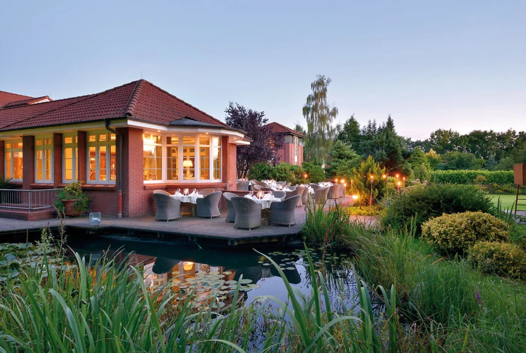 Köhlers Forsthaus Wellness‑ und Genusshotel am Waldrand in Aurich, umgeben von parkähnlichem Garten und kleinem See für erholsame Auszeiten in Ostfriesland.