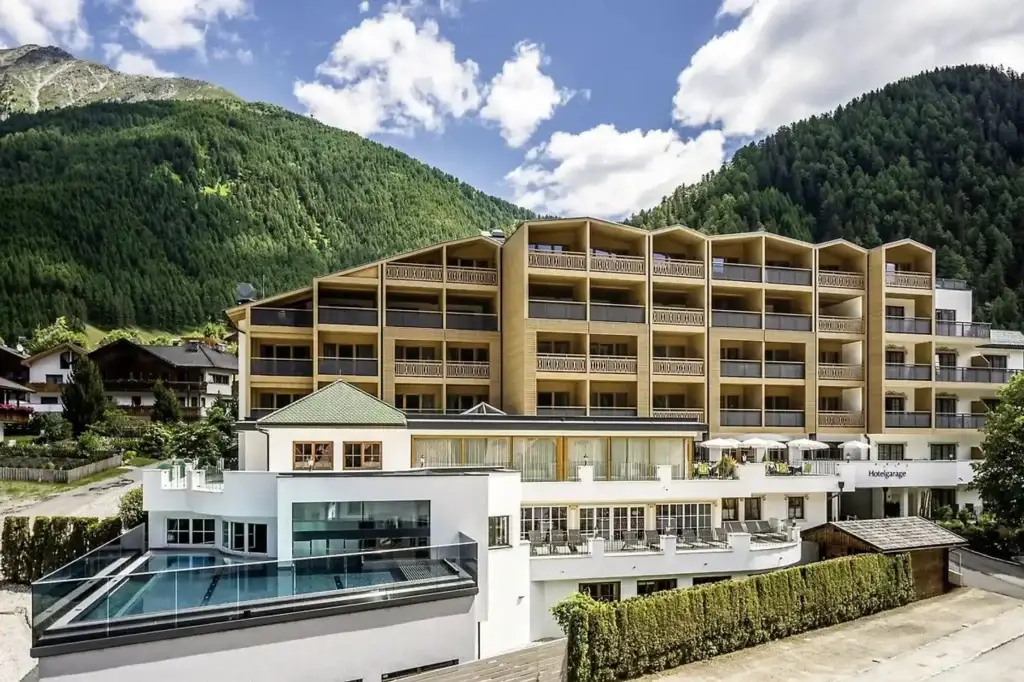 "Außenansicht eines Hotels mit heller Fassade, Pool und Terrasse in Vals, Südtirol vor Alpenkulisse